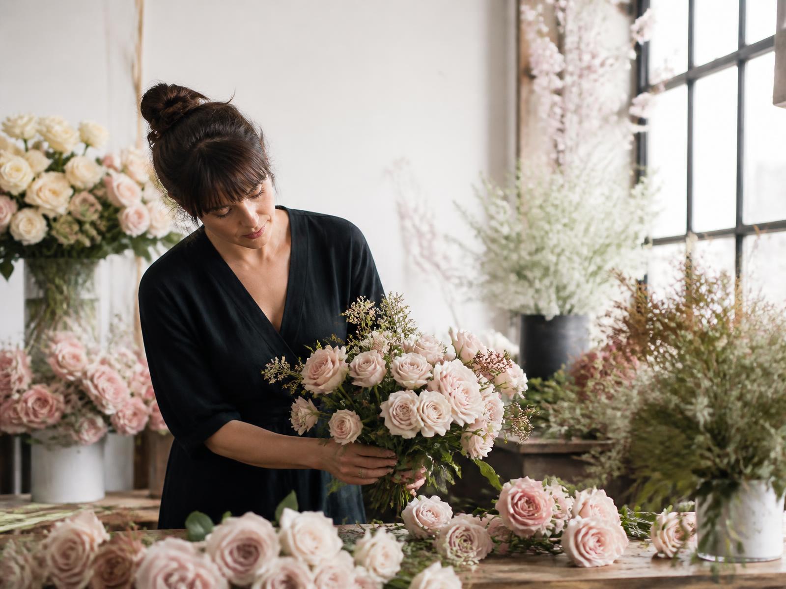 A wedding florist arranging blush roses in a light-filled studio